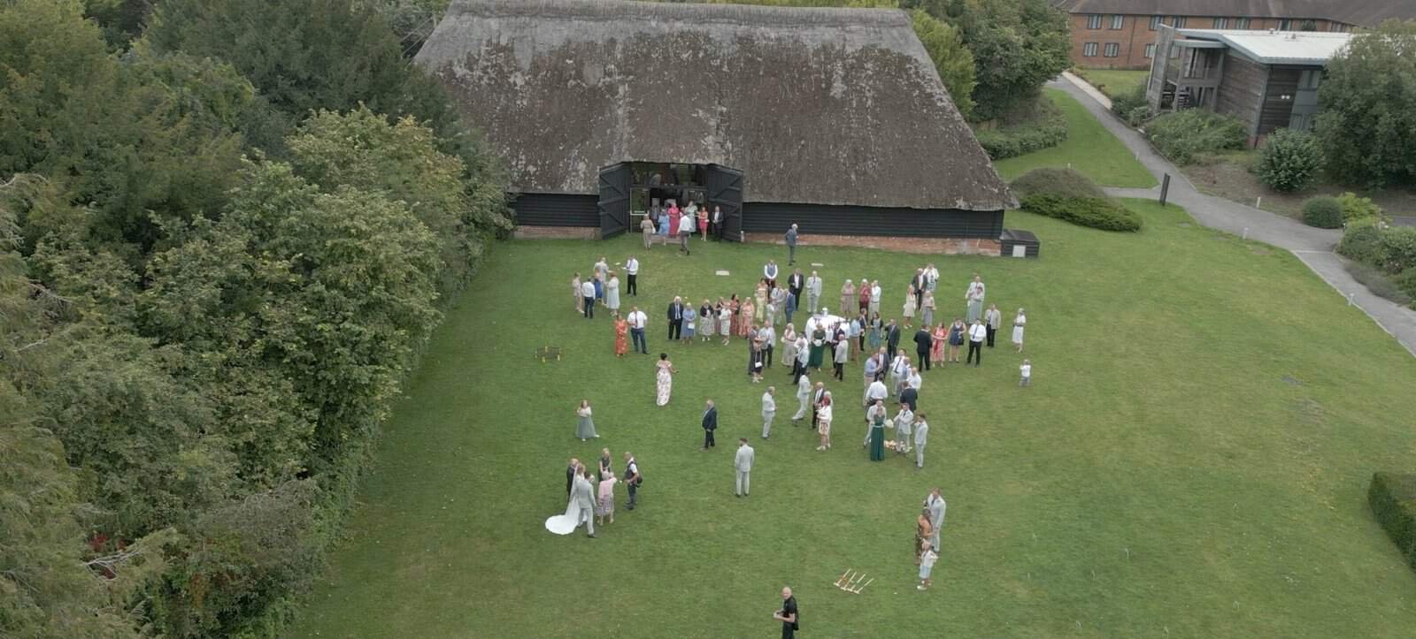 Outdoor wedding gathering near thatched roof structure.