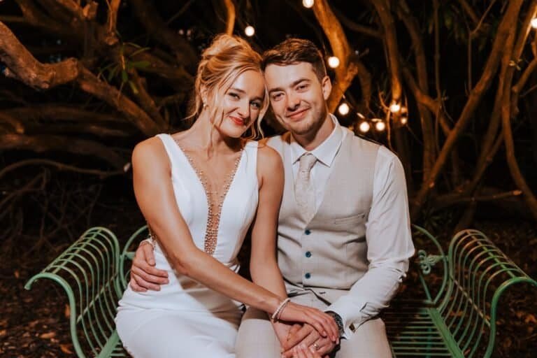Elegant couple seated on garden bench at night.