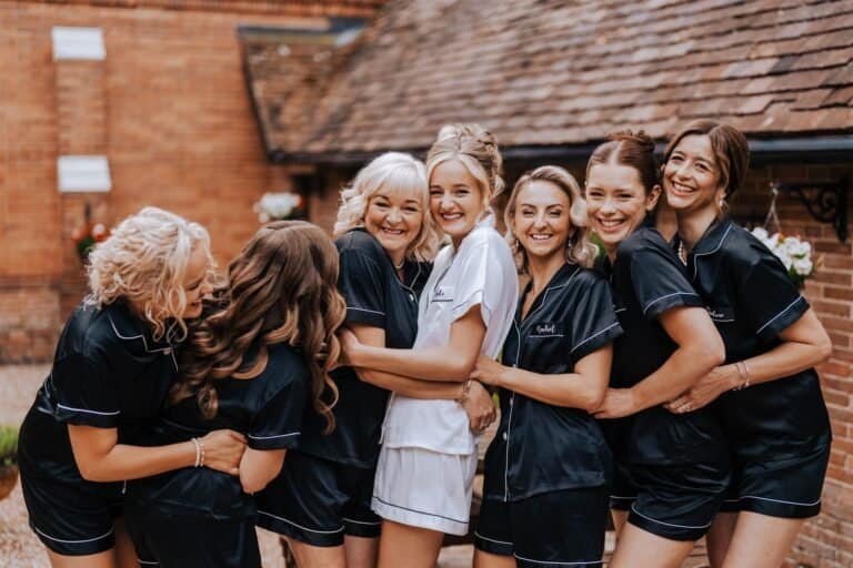 Bridesmaids in matching black pyjamas laughing together outside on the wedding morning