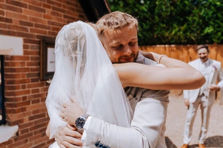 Groom holding the bride close, her veil lifted over his shoulder
