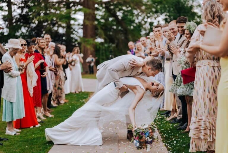 Groom dipping the bride as guests line the path and cheer at Highley Manor