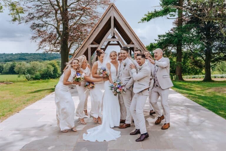 Bride, groom, bridesmaids and groomsmen walking together outside the chapel at Highley Manor