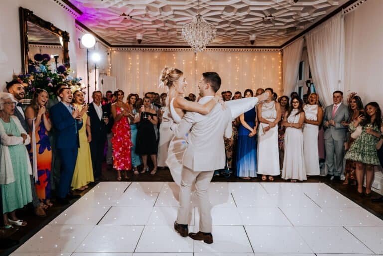 Dancing couple at wedding reception with guests in elegant venue, capturing joyful celebration and entertainment.