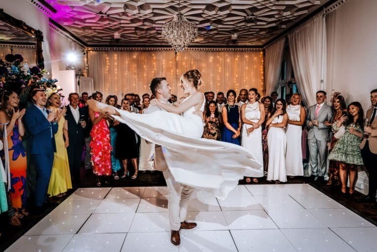 Bride and groom's first dance at wedding reception with friends and family, elegant venue with fairy lights.