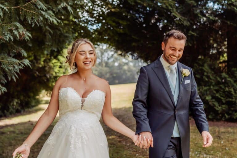 Bride and groom walking hand in hand and laughing in the grounds