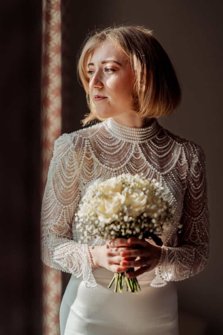 Bride in window light holding her bouquet before the ceremony