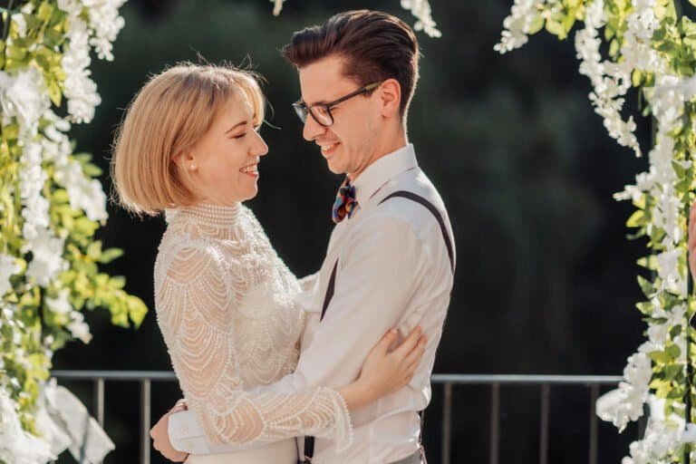 Bride and groom together beneath a white floral arch