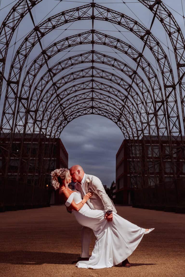 Groom dipping the bride beneath a lit archway at The Village, Farnborough