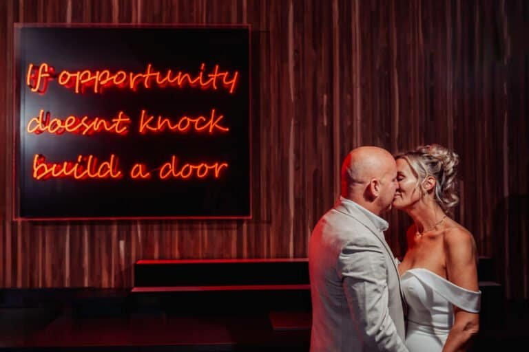 Bride and groom kissing in front of a neon sign at their evening reception