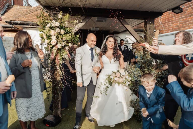 Newlyweds walking hand in hand through confetti under a floral arch